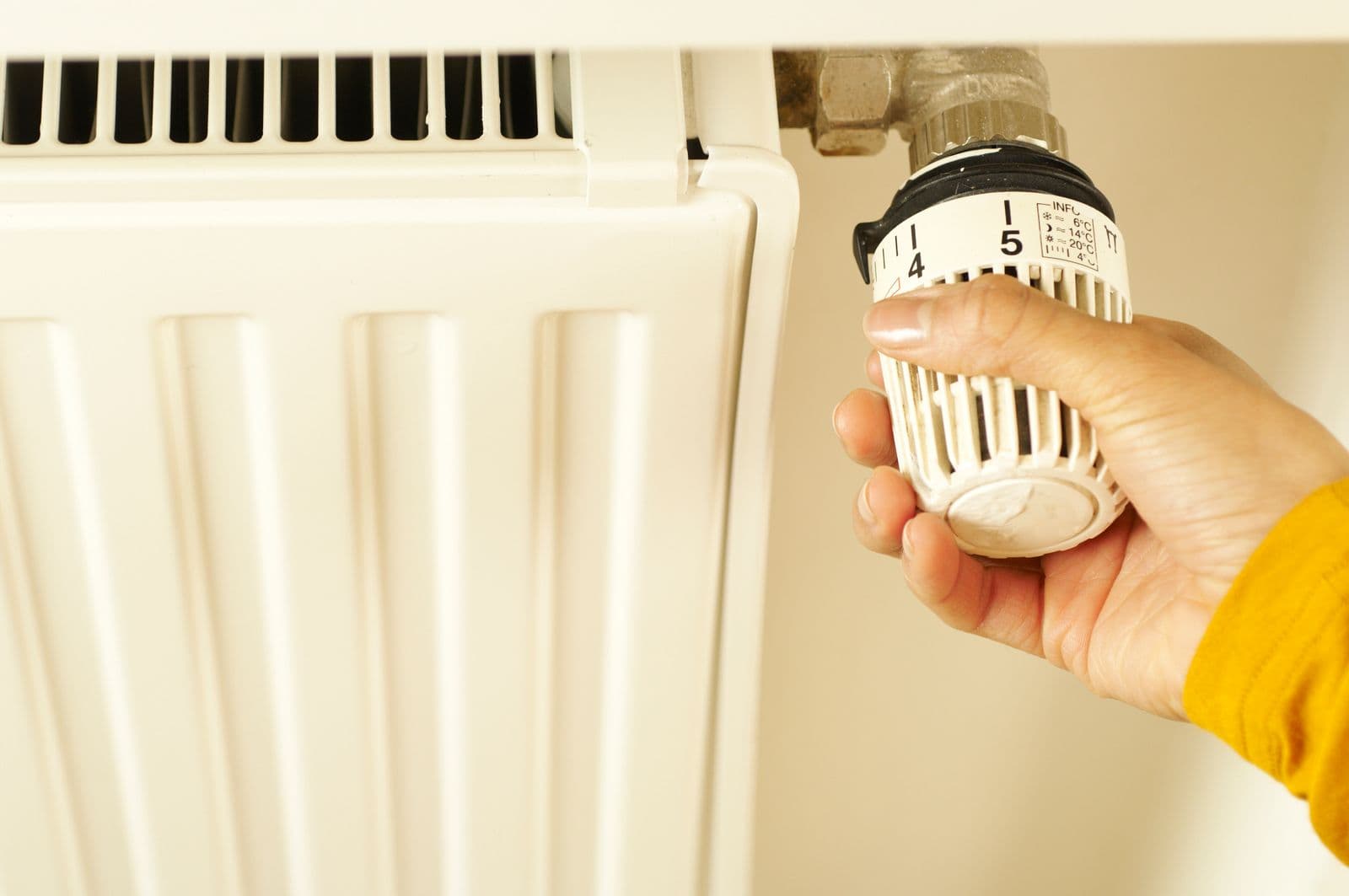 Una mano gira la válvula termostática de un radiador blanco.